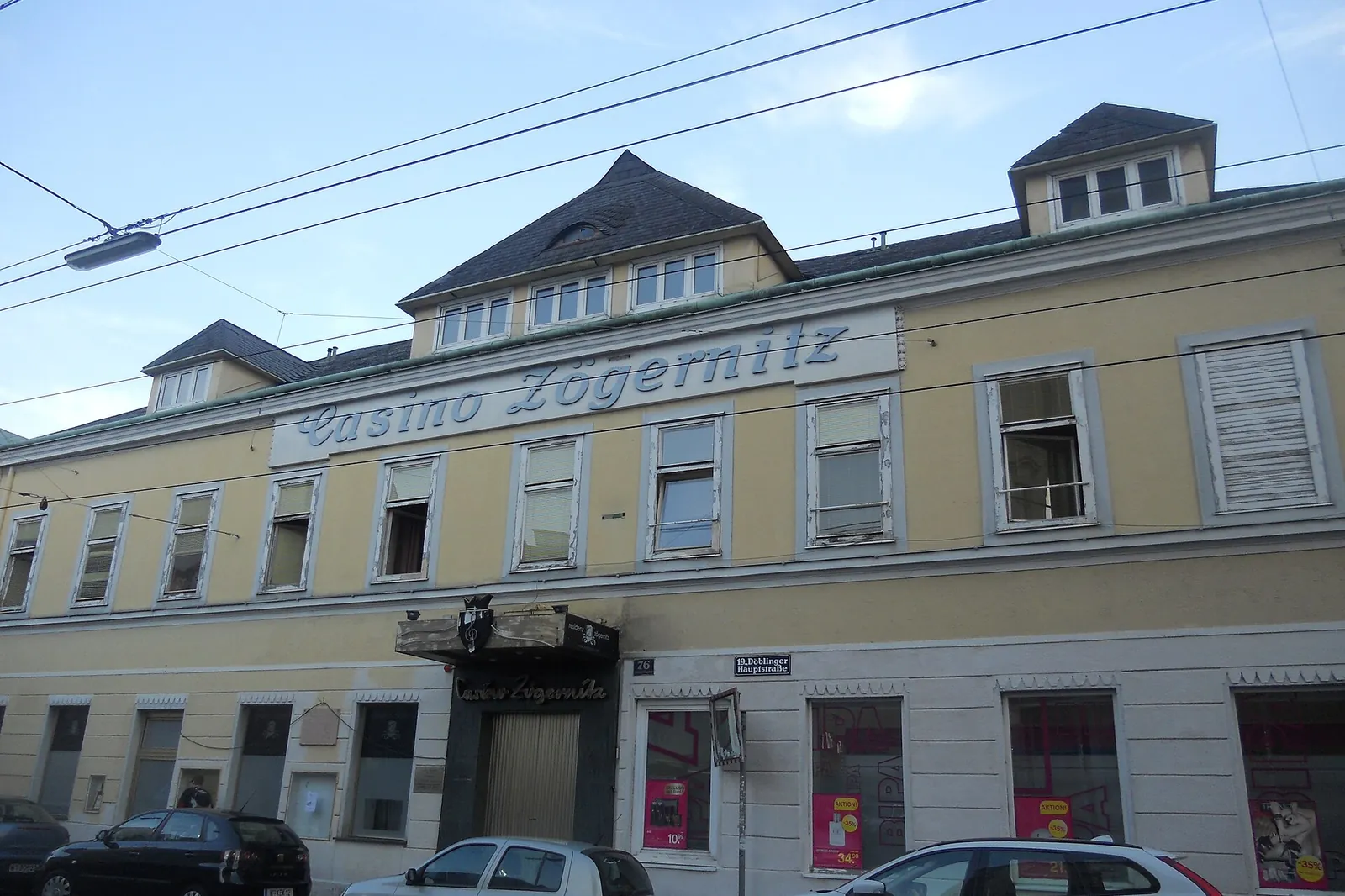 The yellow and cream façade of the former Casino Zögernitz on Döblinger Hauptstraße, with tram wires overhead and the name in raised letters below the roofline